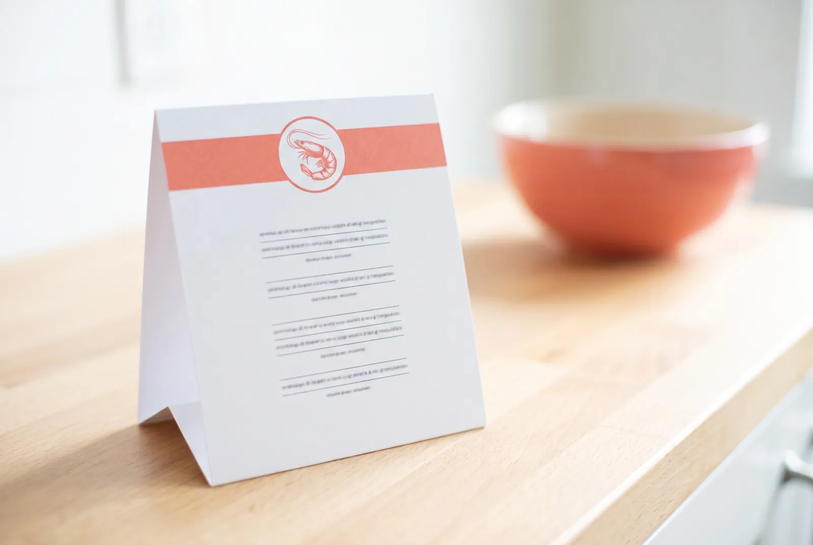 White table tent card with coral band and shrimp roundel on the counter