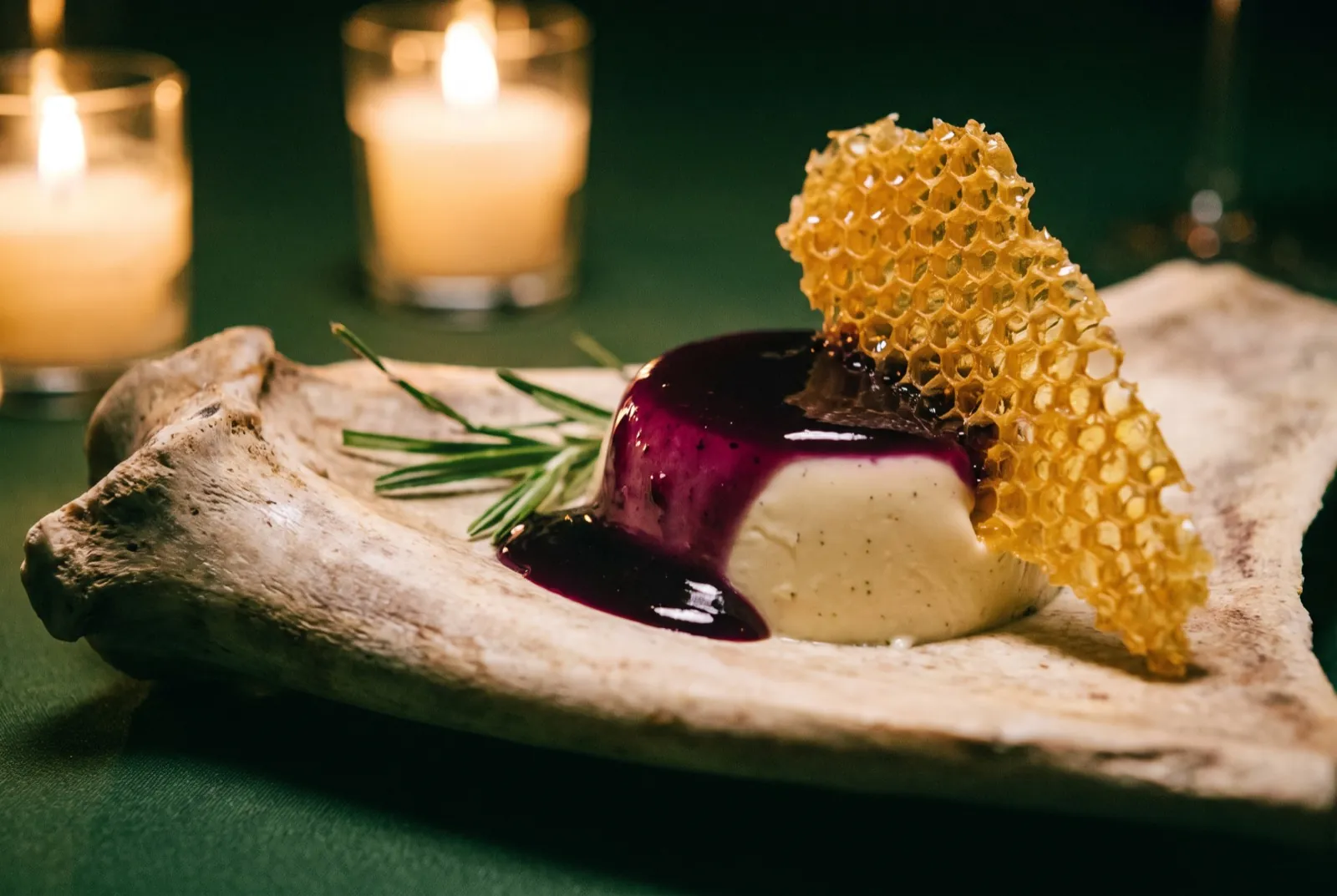 Sweetgrass panna cotta with muscadine and a honeycomb shard on driftwood, candlelit